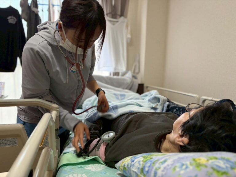 訪問看護師が自宅の介護ベッドで利用者様の血圧を測っている様子