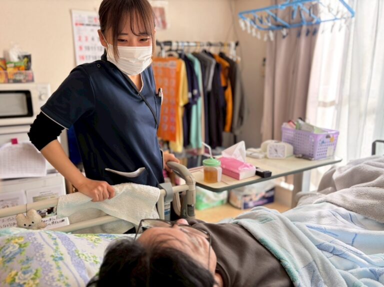 訪問先の居室で、看護師がベッドの利用者様にタオルを使ってケアをしている