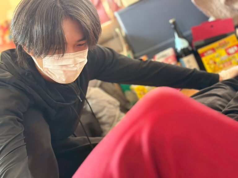 訪問先の居間で、利用者様の脚に手を添えて施術している理学療法士