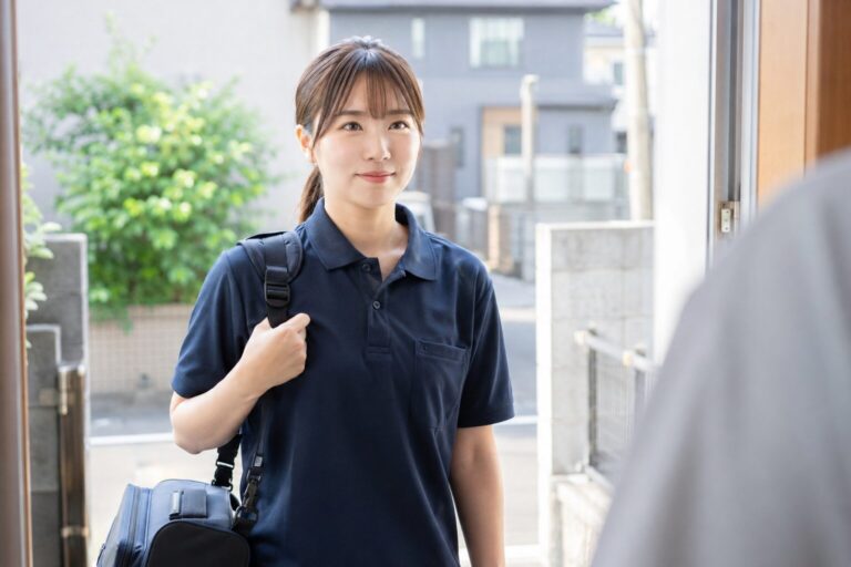 訪問先の玄関先で、かばんを肩に掛けて笑顔で挨拶する訪問看護のスタッフ
