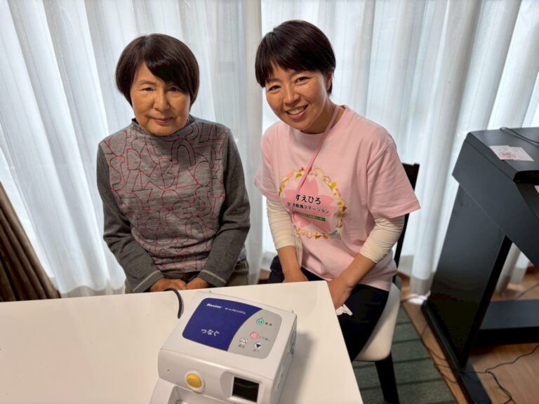 腹膜透析の機械の前で、利用者様とすえひろのスタッフが並んで笑顔で写っている