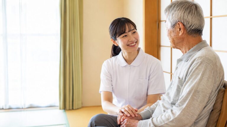 和室で、看護師が高齢の男性の手を取り笑顔で話しかけている